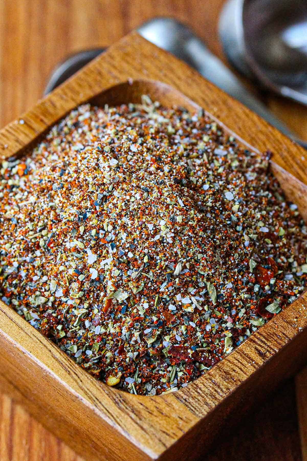A small square wooden bowl filled with homemade taco seasoning sitting on a wooden cutting board.