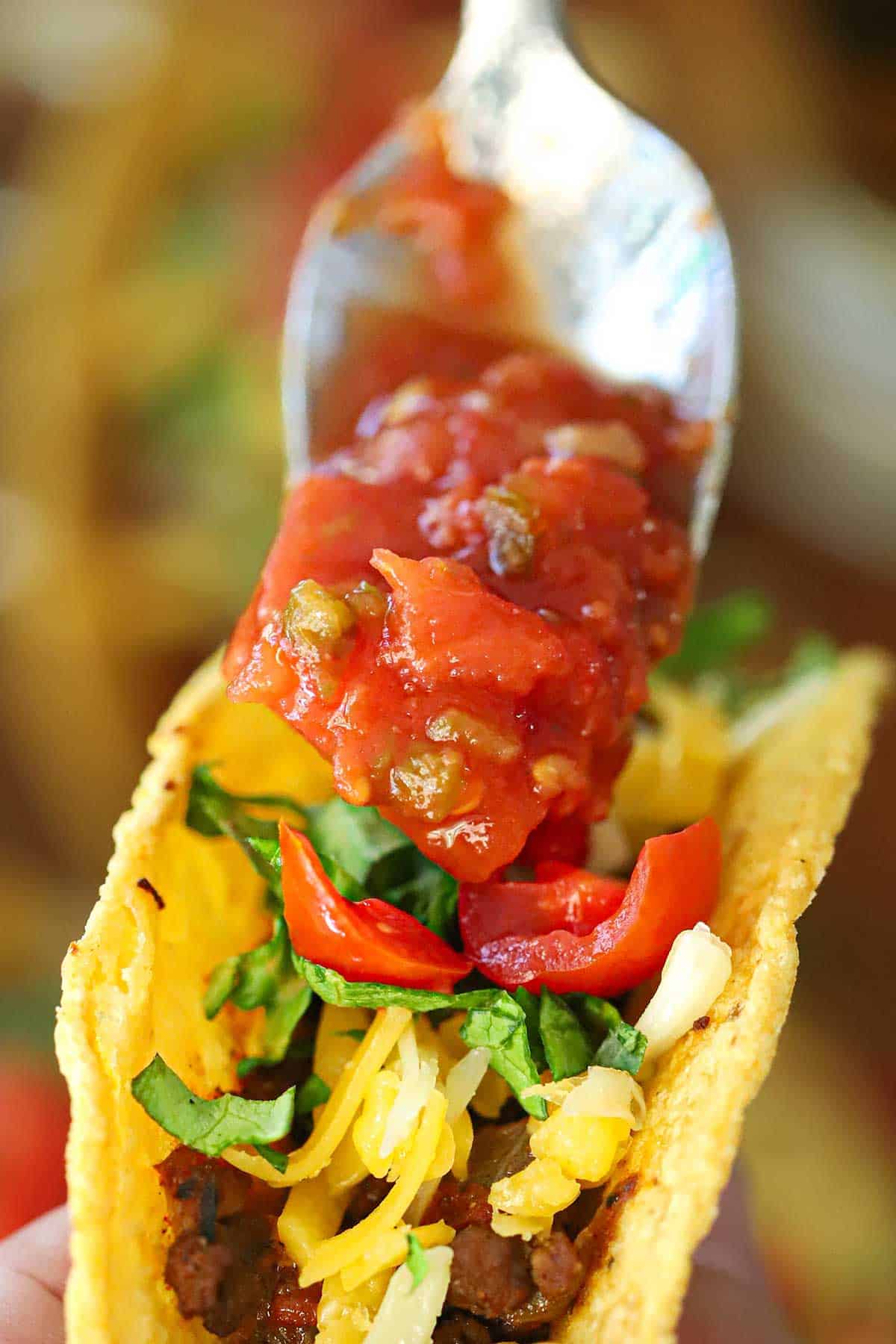 A person using a spoon to top a beef taco with restaurant-style salsa.