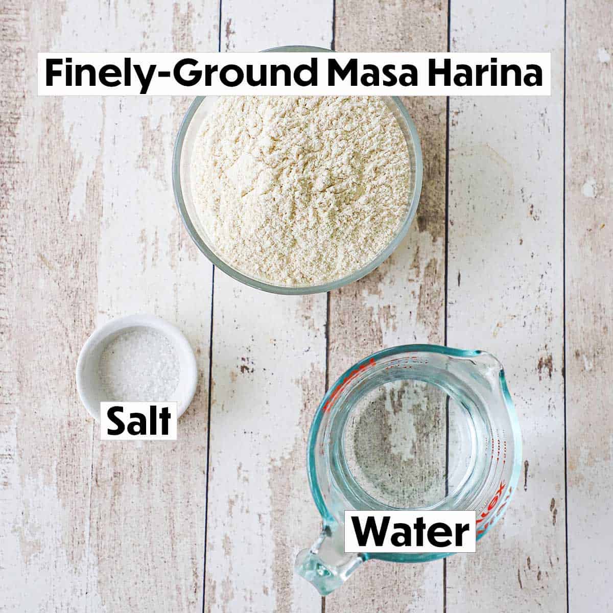 A arrangement three ingredients for homemade corn tortillas on a white background including finely-ground masa harina, salt, and water in a glass measuring cup.
