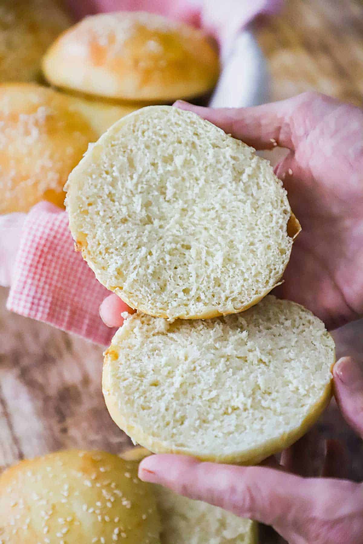 Person holding a homemade hamburger bun that has been split in half and the fluffy inside of the bun is visible.