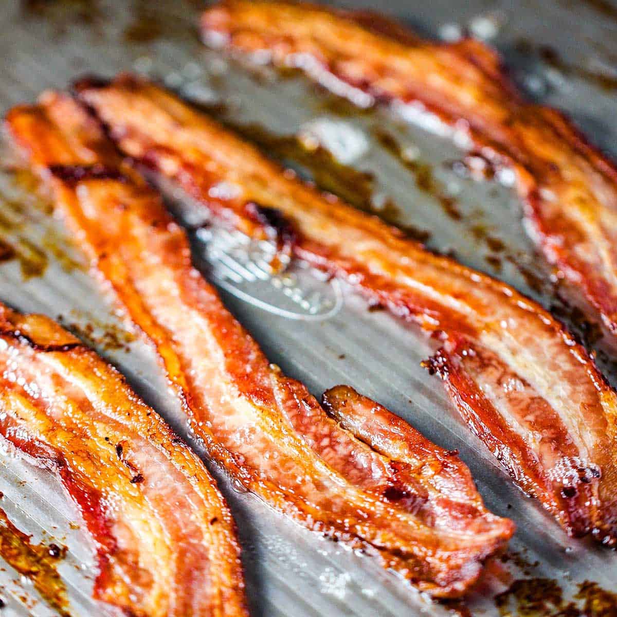 Strips of freshly baked crispy bacon on a metal baking sheet pan.