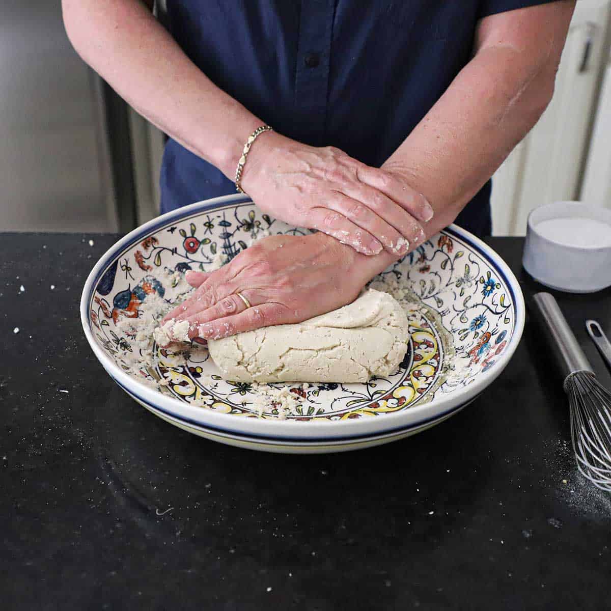 A person using the palm of his hand to knead corn flour in a large shallow bowl for homemade corn tortillas.