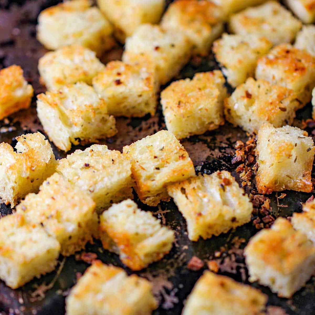 Freshly toasted croutons on a scratched metal baking pan.