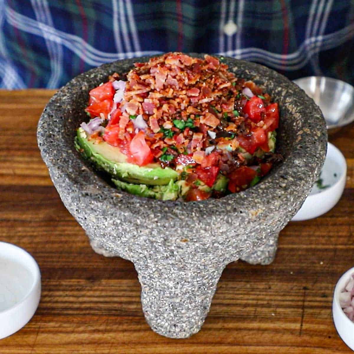 A molcajete sitting on a wooden cutting board filled with the un-mixed ingredients for best-ever guacamole.