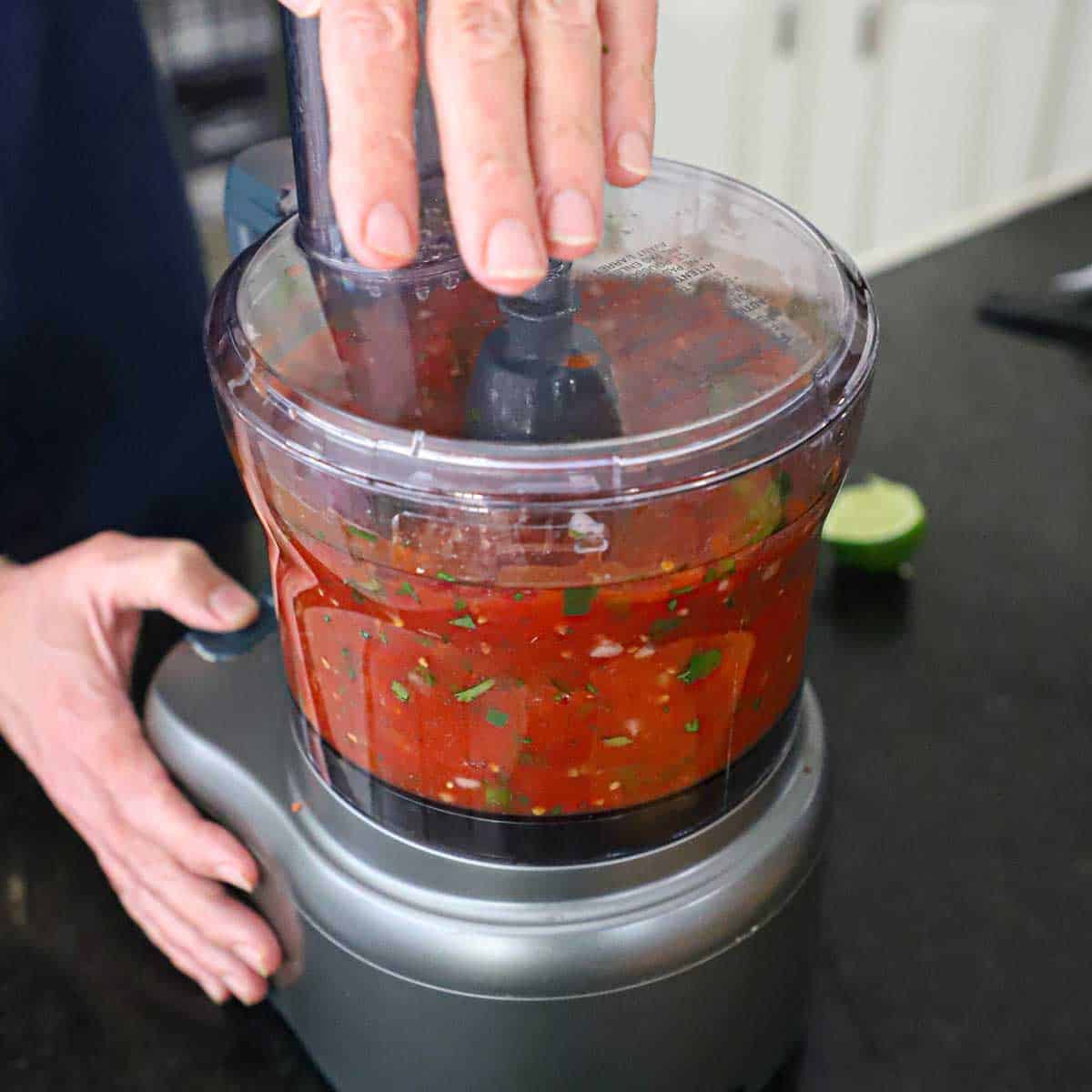Person pulsing a food processor while holding the lid in place with freshly-made restaurant-style sals in it.