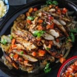 Tex-Mex chicken fajitas sitting on large oval fajita pan and topped with fresh pico de gallo and chopped cilantro with bowls of grated cheese and pico de gallo nearby.