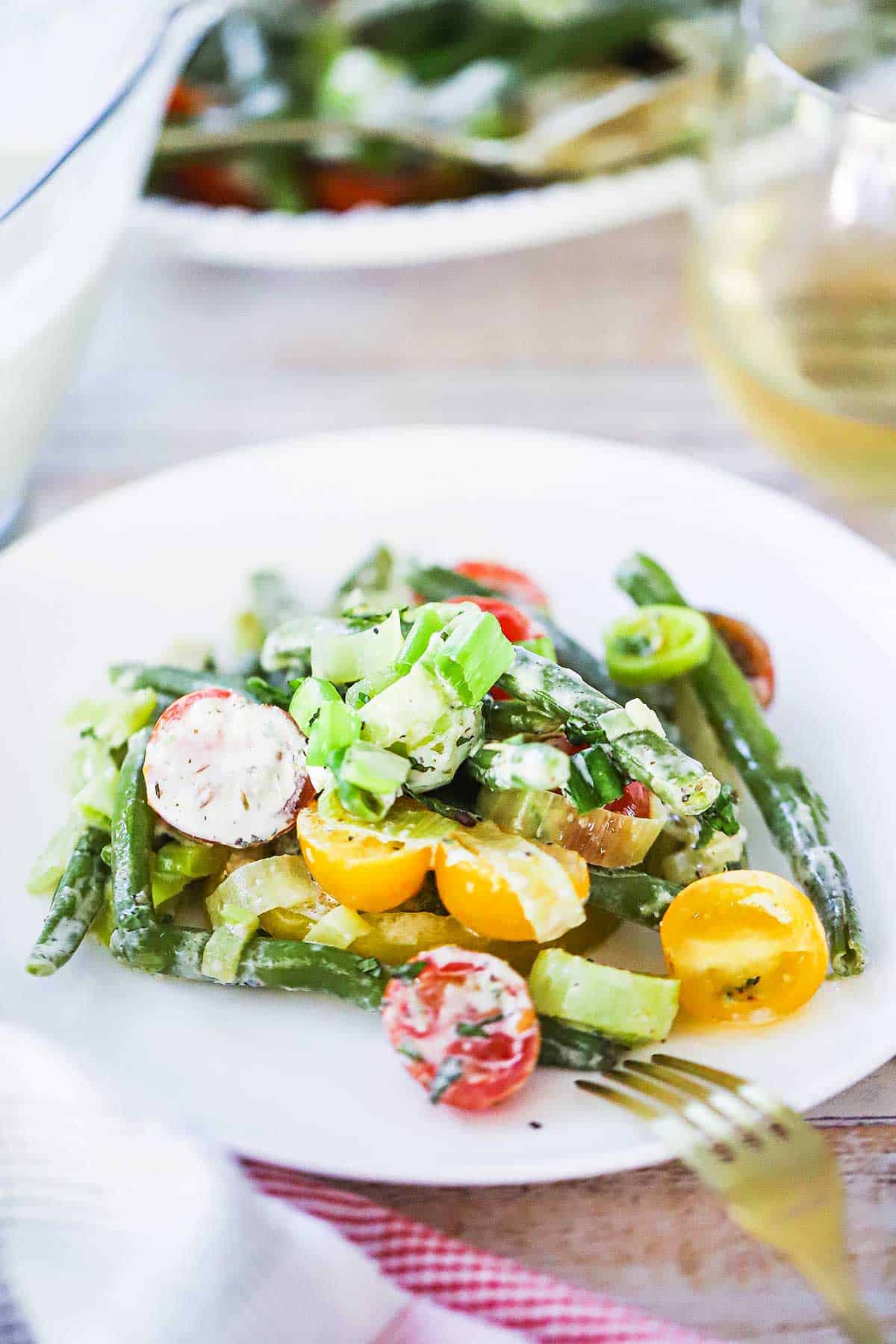 A white salad plate filled with an individual serving of green bean and tomato salad with scallion buttermilk dressing on top.