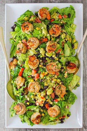 A large rectangular white platter filled with a grilled shrimp salad with cilantro-lime dressing along with grilled corn, black beans, chopped lettuce, all on torn pieces of romaine lettuce.