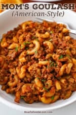 A white dinner bowl filled with a serving of Mom's goulash (American-style) with finely chopped parsley sprinkled on top.