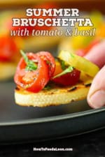 A person placing a Summer bruschetta with tomato and basil on a black plate next to more burshetta.