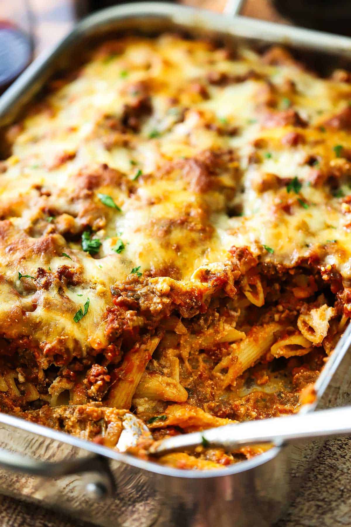 A stainless steel lasagna pan filled with best-ever baked ziti with a portion of it missing revealing the pasta and meat sauce in side the ziti.