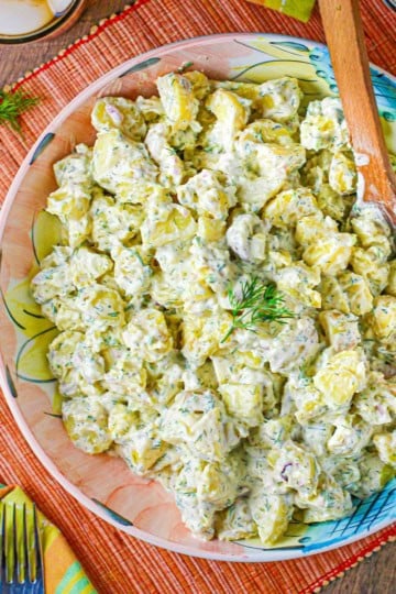 An overhead view of best-ever potato salad in a large colorful serving bowl with a sprig of fresh dill resting on top.