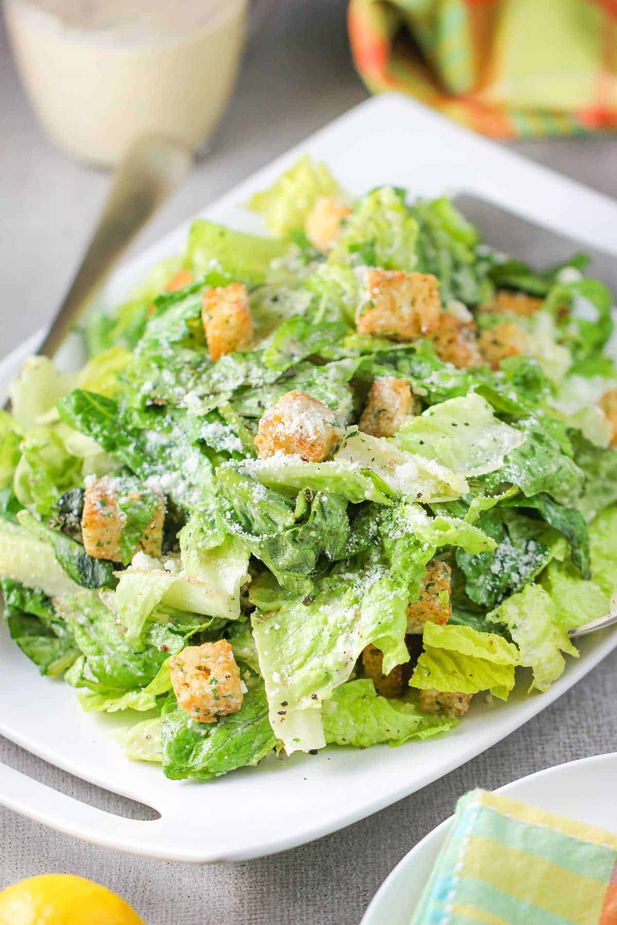 A classic Caesar salad served family-style on a large white platter topped with homemade croutons and grated Parmesan cheese.