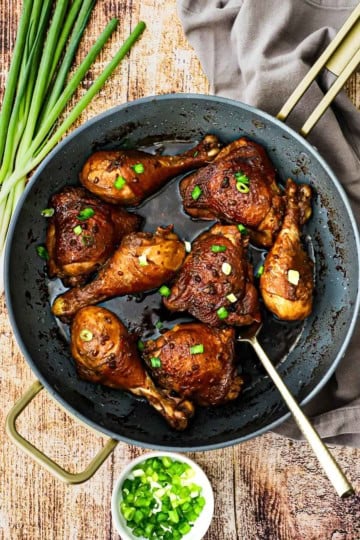 A large non-stick skillet filled with Filipino adobo chicken with a thick sauce over the chicken and in the bottom of the pan and topped with chopped scallions.