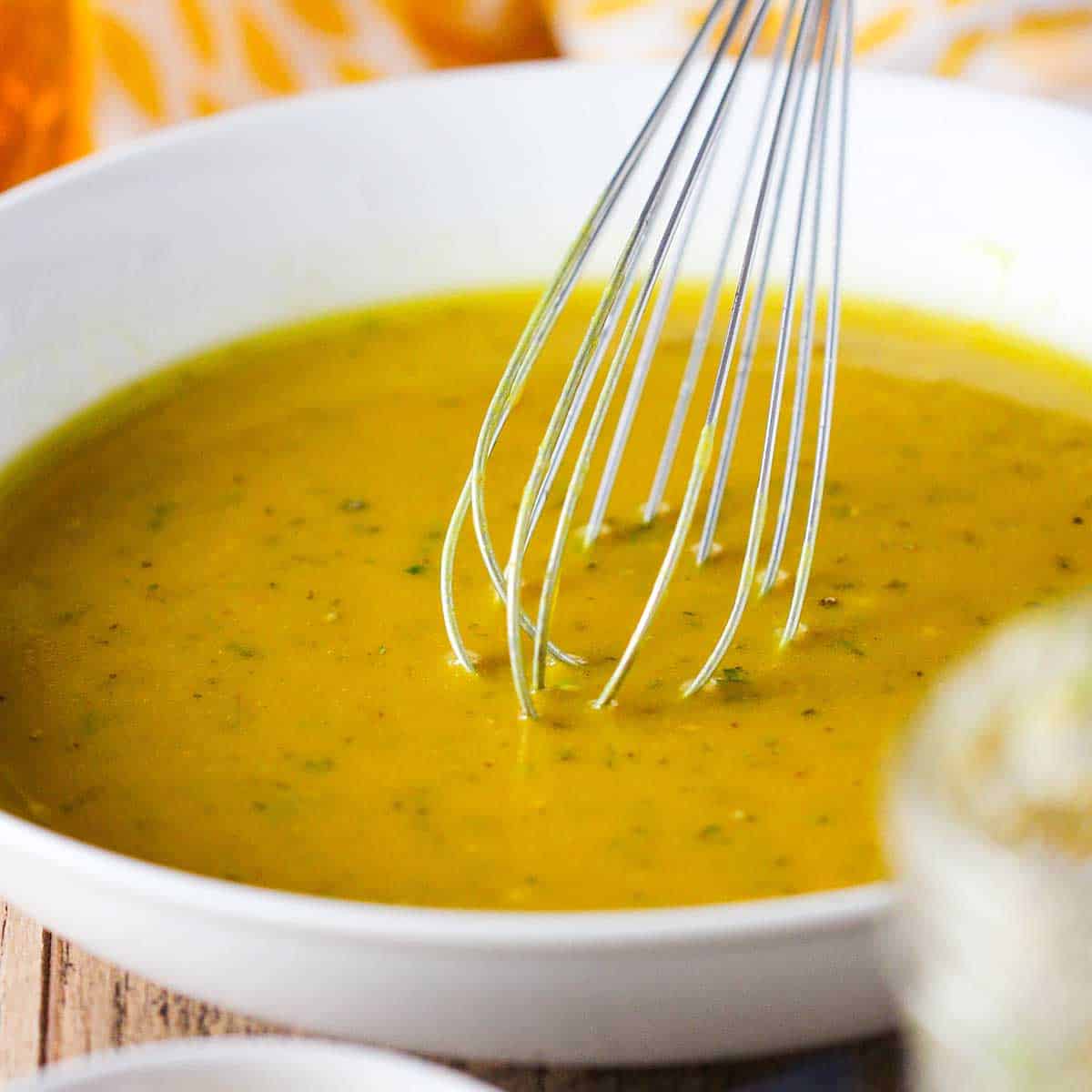 A person using a whisk to stir a honey mustard sauce and marinade in a shallow white bowl.