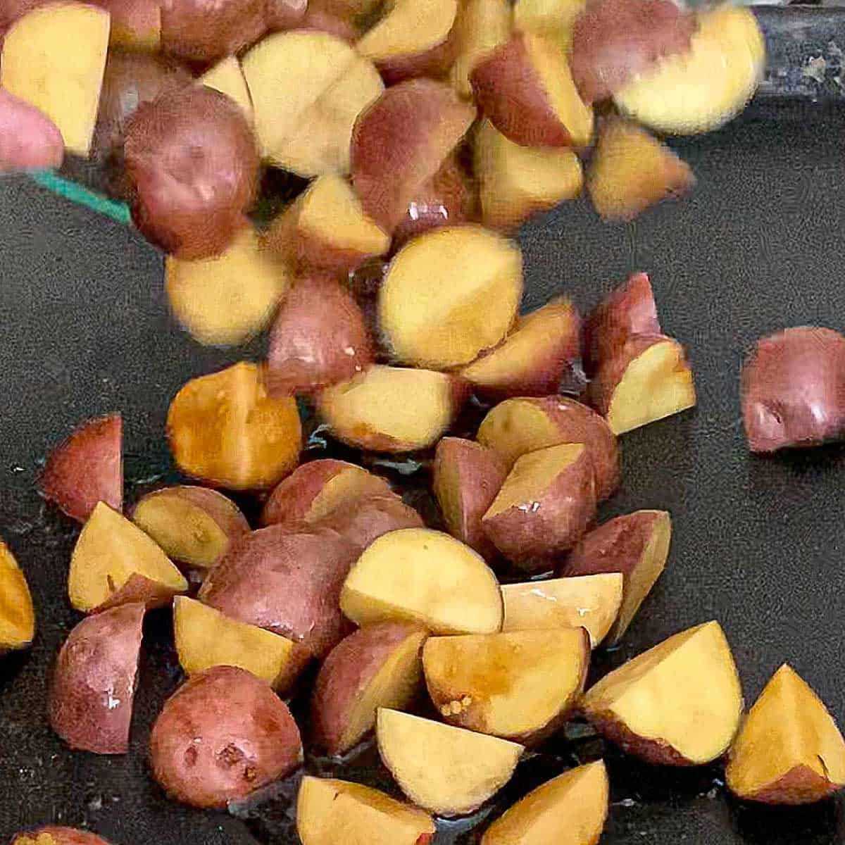 New potatoes that have been cut in half being placed on a black baking sheet pan.