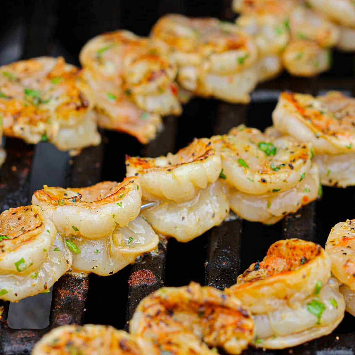 Three rows of marinated shrimp that are being grilled on the grate of a gas grill.