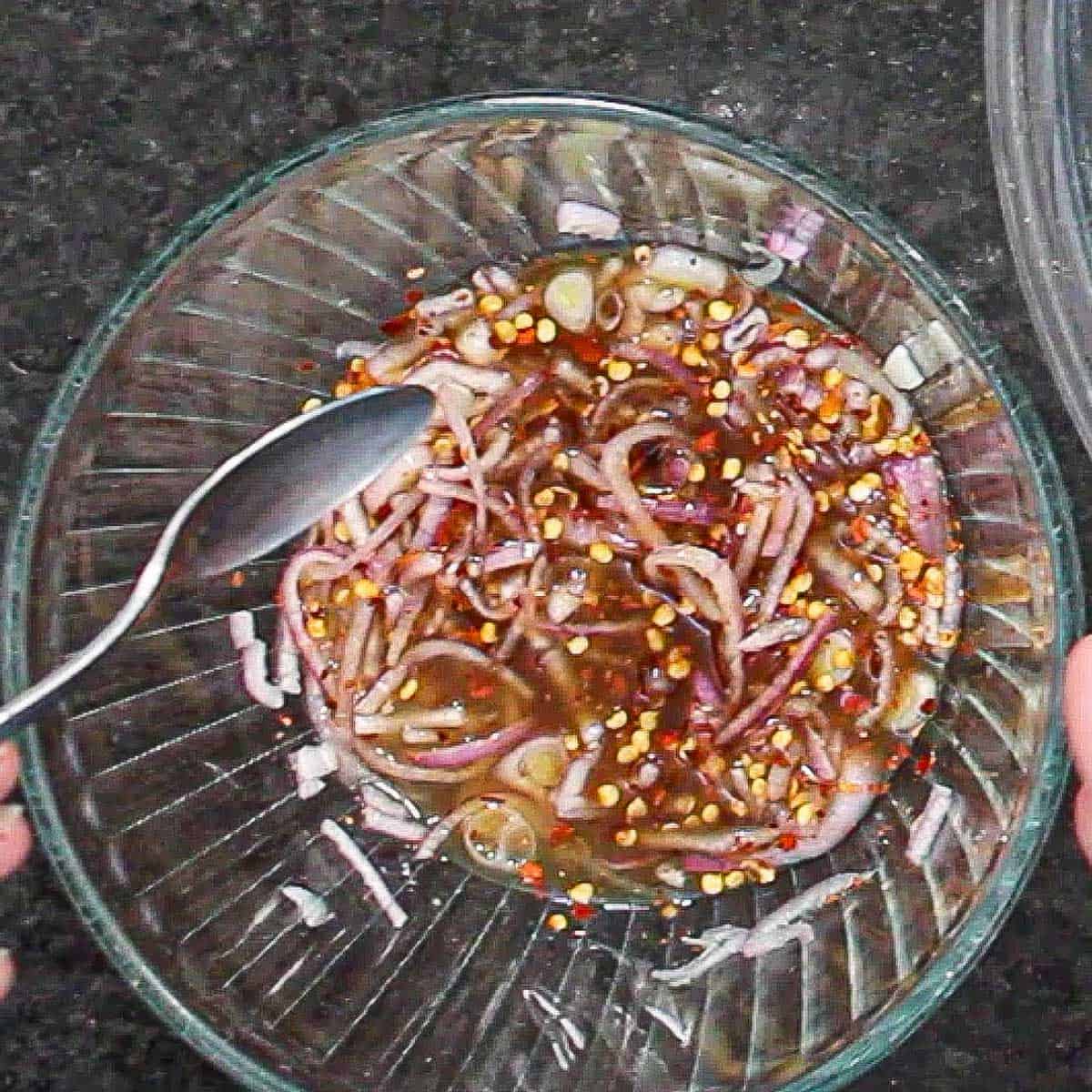A person holding a spoon over a bowl filled with a marinade for Thai beef salad.
