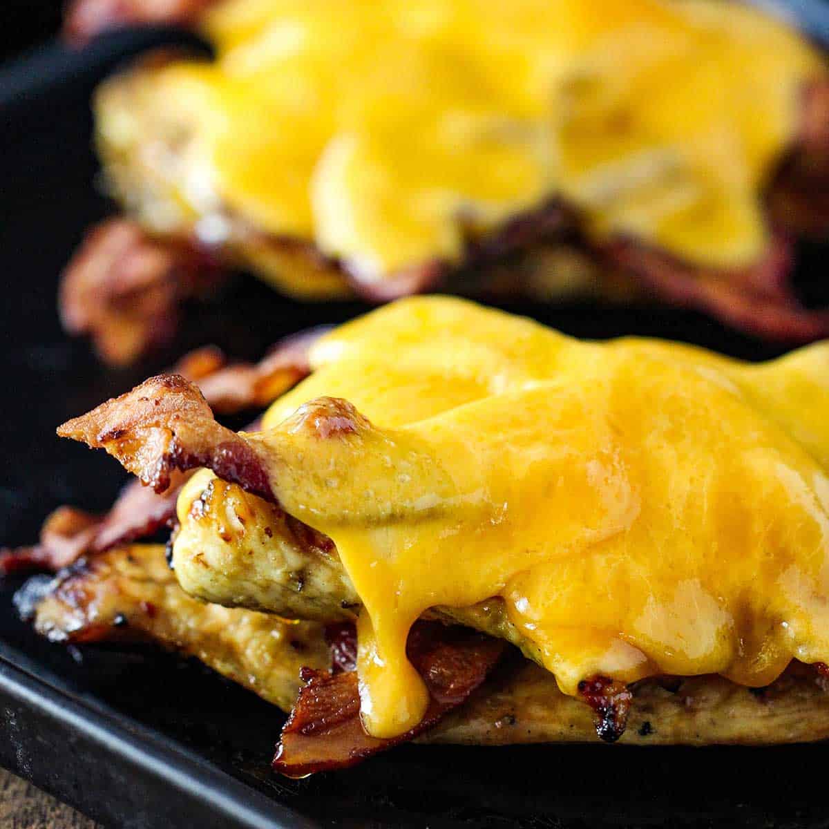 A close-up view of two layers of grilled chicken and crispy bacon that are topped with melty slices of cheddar cheese.