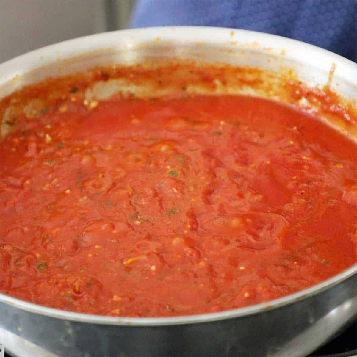 A large stainless steel skillet filled with simmering homemade marinara sauce.