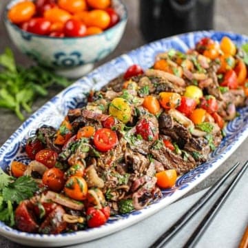 A long, blue and white oval platter filled with a large serving of Thai beef salad with two chopsticks nearby.