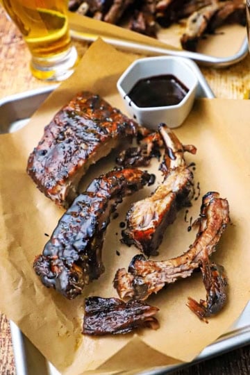 A small baking pan lined with brown paper and topped with balsamic glazed baby back ribs with a small bowl filled with the glaze nearby.