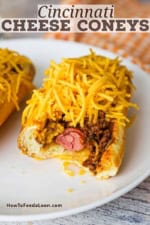 A half-eaten Cincinnati cheese coney resting on a white dinner plate next to another untouched Coney.