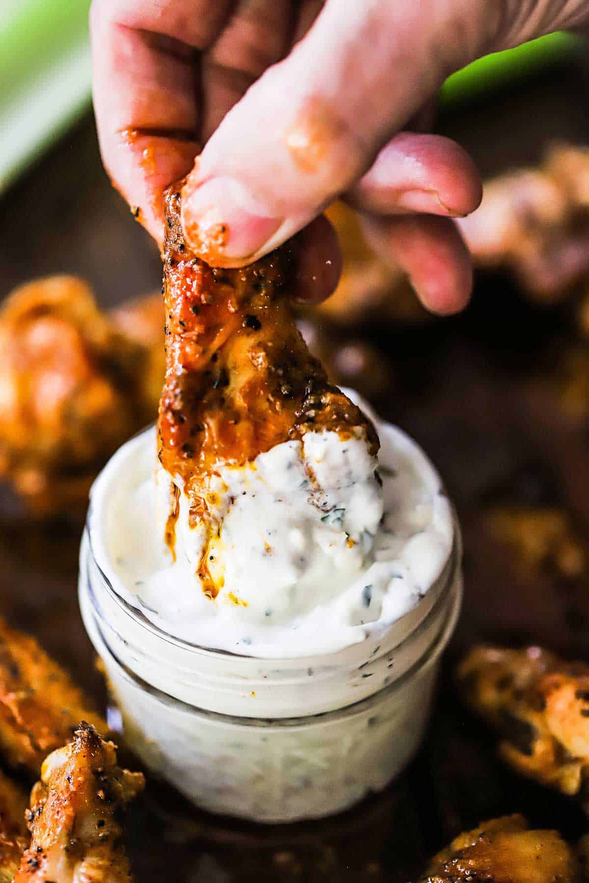 A person plunging a grilled buffalo wing into a small glass jar filled with homemade blue cheese dressing.