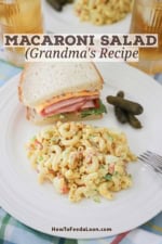 A white dinner plate filled with a serving of classic macaroni salad and half of a ham sandwich with three small pickles also sitting on the plate.