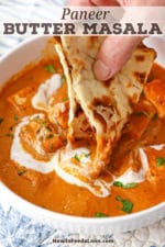 A person plunging a folded piece of naan into a white bowl filled with a serving of panner butter masala.