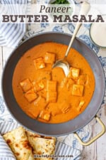 A large non-stick skillet filled with paneer butter masala with a gold serving spoon inserted into the pan.
