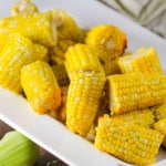 Slow-cooker corn on the cob cutlets resting in a large white ceramic platter with fresh ears of corn nearby.