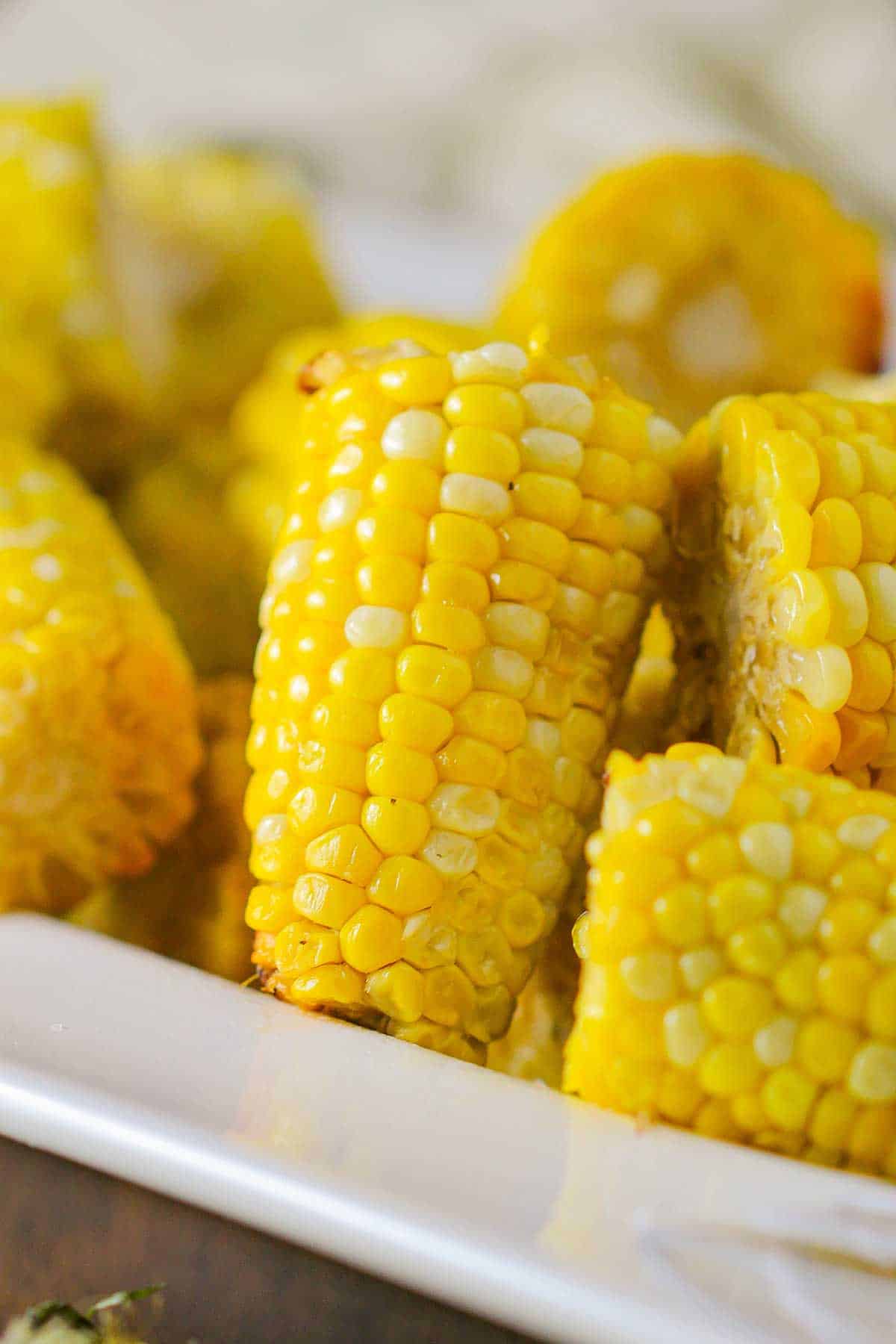 A close-up view of slow cooker corn on the cob cutlets stacked on each other in a white platter with a wide lip.