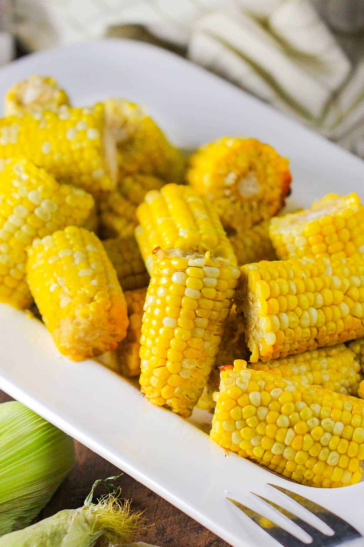 Slow-cooker corn on the cob cutlets resting in a large white ceramic platter with fresh ears of corn nearby.