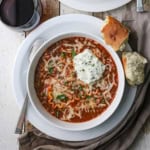 An overhead view a bow filled with a serving of slow cooker lasagna soup with a dollop of ricotta cheese off to the side and two piece of Italian bread next to the bowl.