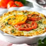 A close-up view of a tomato pie in a white ceramic pie dish with three colorful baked heirloom tomato slices on top with chopped parsley sprinkled on the surface of the pie.