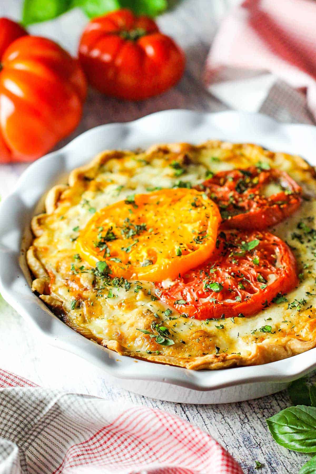 An untouched tomato pie in a white ceramic pie dish with three colorful baked heirloom tomatoes on the top of the pie.