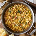 An overhead view of a large filled with One-Pot Marry Me Chicken Pasta including cooked pasta shells, bites of chicken, sun-dried tomatoes, wilted spinach, all in a creamy Tuscan sauce.