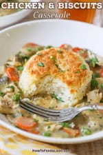 A half-eaten biscuit from a white bowl filled with a serving of chicken and biscuits casserole with a fork resting in the bowl.