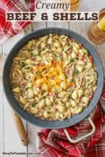 An overhead view of a large skillet filled with creamy beef and shells with melty shredded cheddar cheese in the center of the pasta.