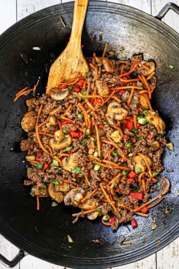An overhead view of a wok filled with fully cooked Korean ground beef stir-fry with a wooden spatula inserted into the side of the food.