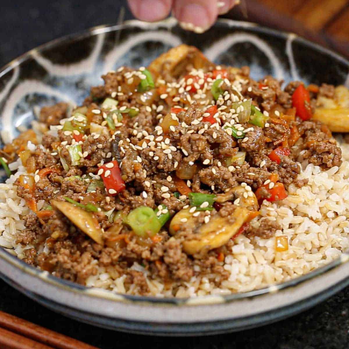 A close-up view of Korean ground beef stir-fry being served over a bed of steamed brown rice in a colorful bowl.