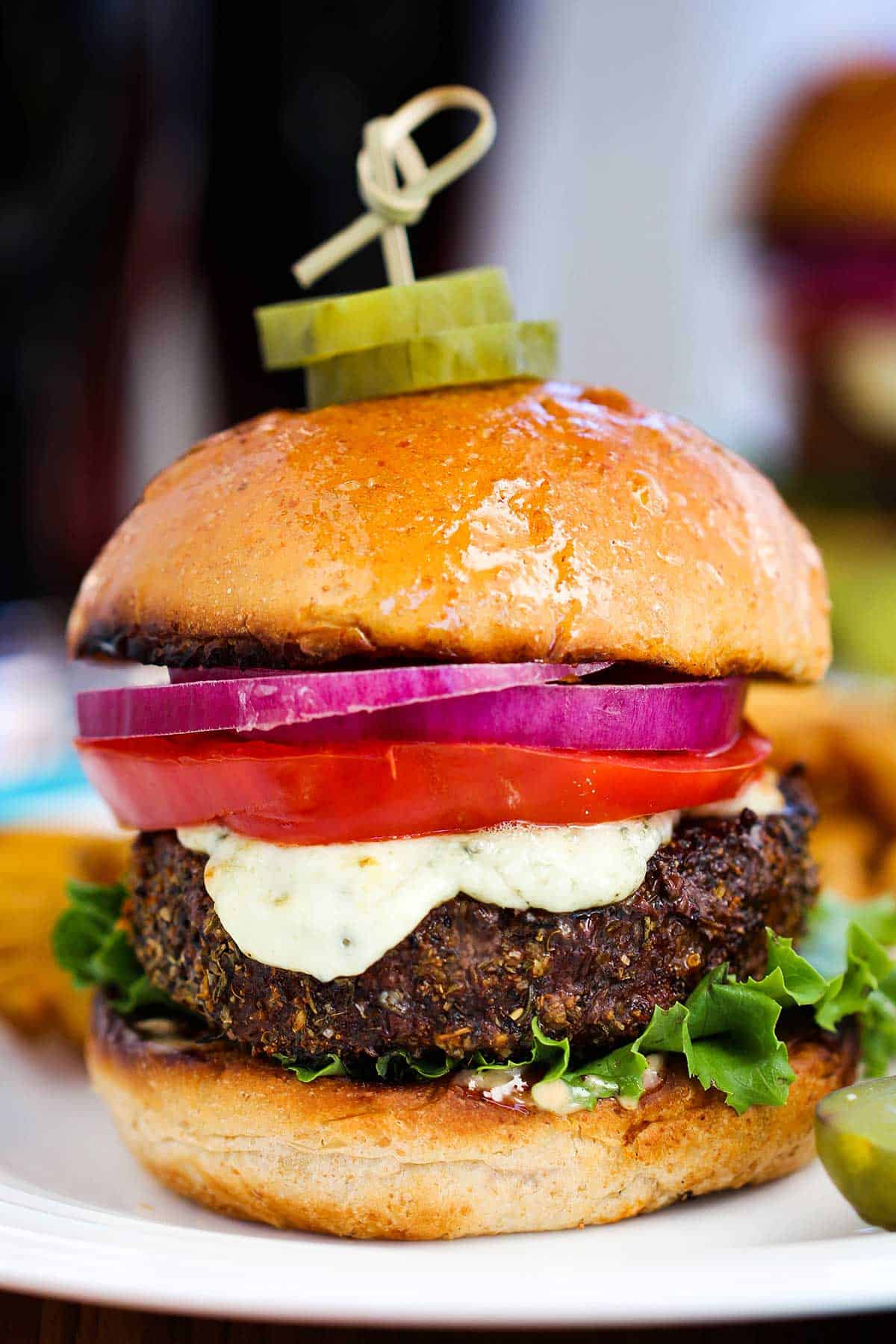 A straight-on view of a black and bleu burger that consists of a blackened hamburger, melty blue cheese, a tomato slice, and two slices of red onion on a toasted bun.