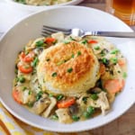 A white bowl filled with an untouched serving of chicken and biscuits with a glass of iced tea just behind the bowl.