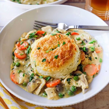 A white bowl filled with an untouched serving of chicken and biscuits with a glass of iced tea just behind the bowl.
