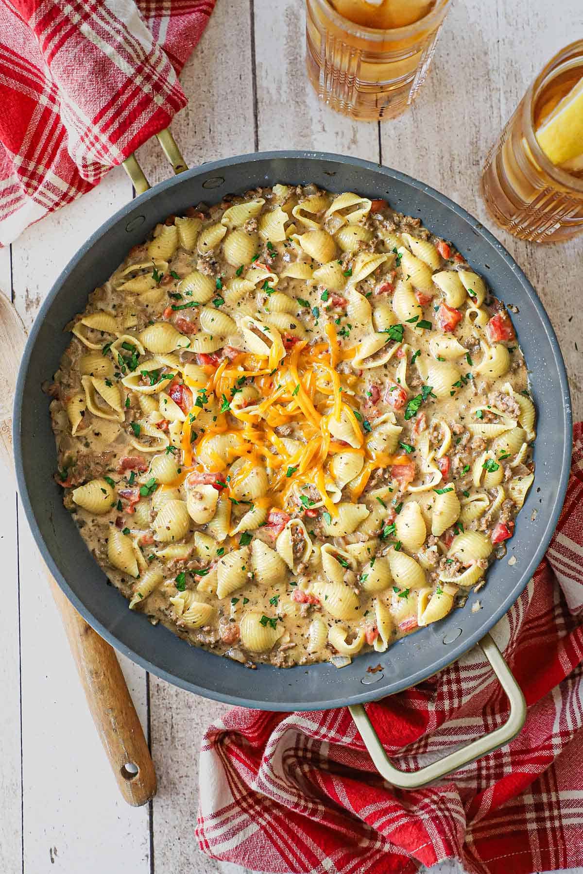 An overhead view of a large skillet filled with creamy beef and shells with melty shredded cheddar cheese in the center of the pasta.
