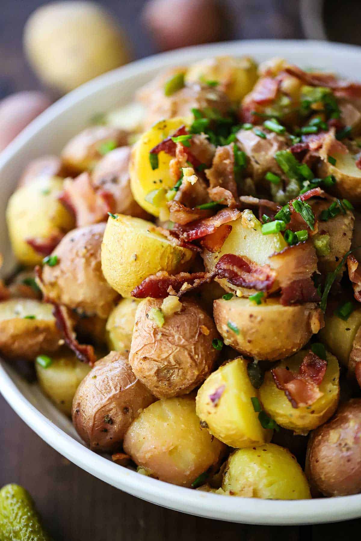 A close-up view of a mound of Best German Potato Salad in a bowl topped with chopped crispy bacon and snipped chives.