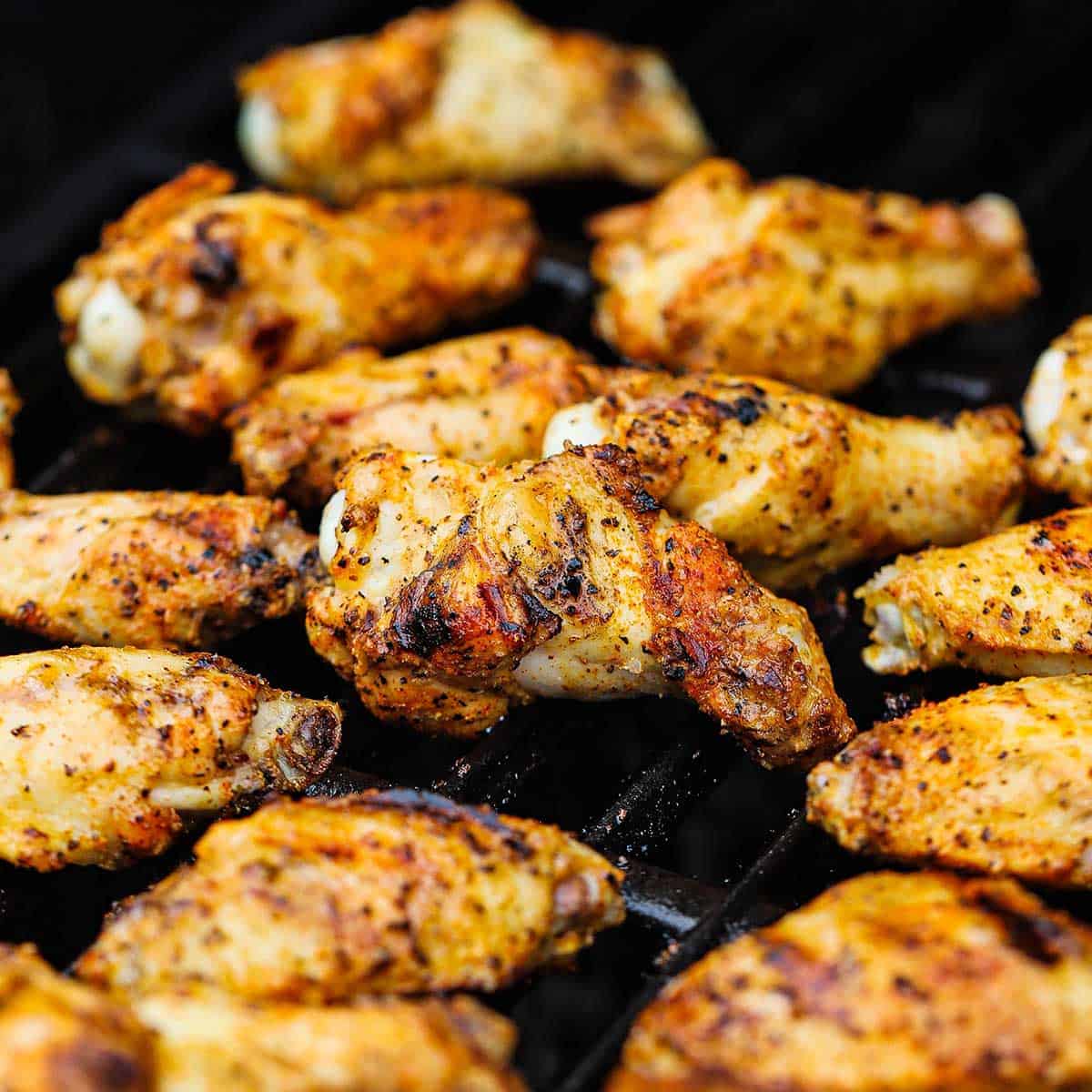 Seasoned chicken wings and drumettes being grilled on the grate of a gas grill.