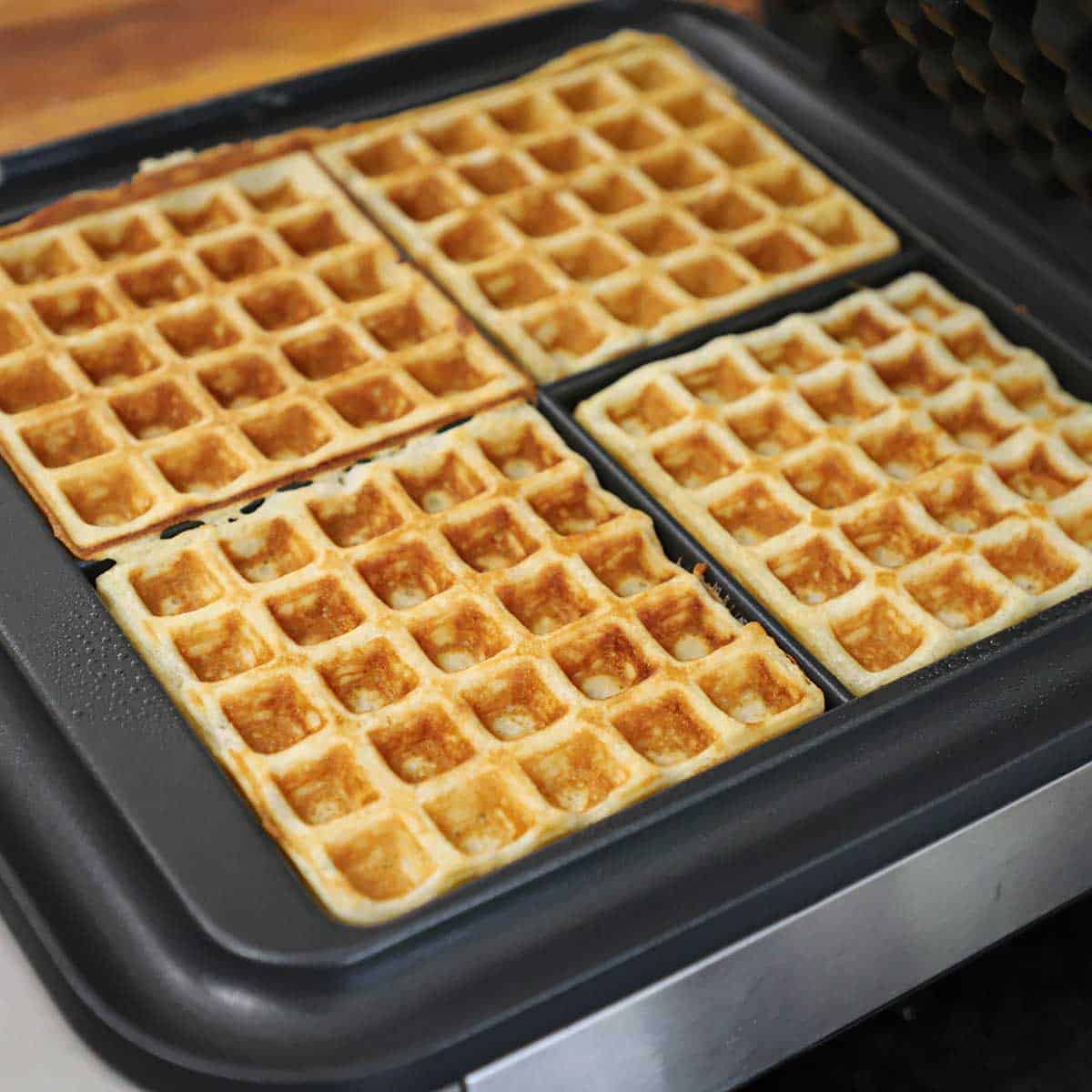 Four freshly prepared waffles resting in a square waffle maker.