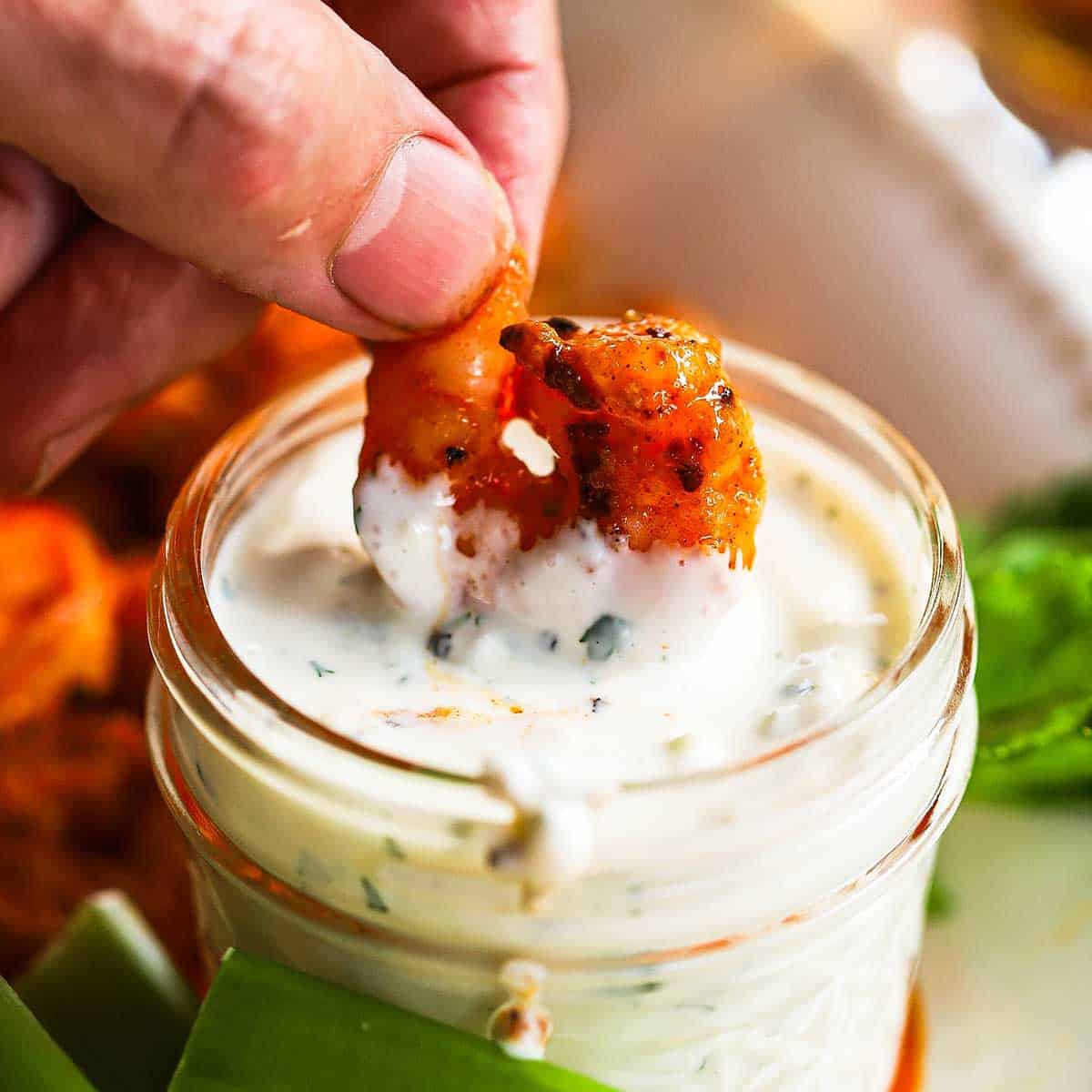 A person plunging a grilled buffalo shrimp into a small jar filled with homemade blue cheese dressing.